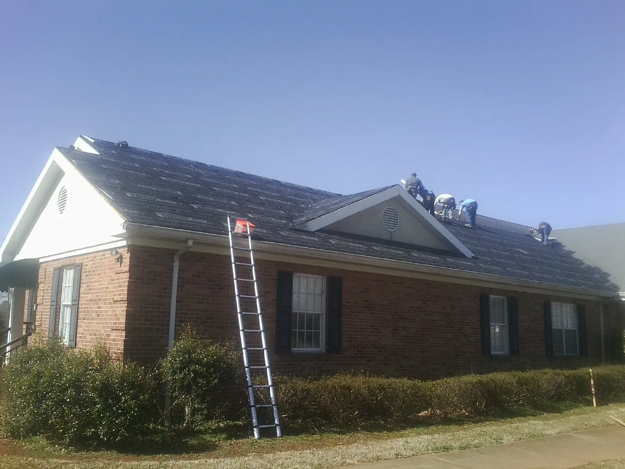 Crew tearing shingles off a brick ranch roof with a ladder set — Metal Roof Repair work by our crew in Shamokin Dam