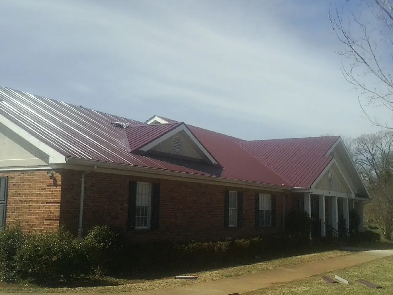 Red metal roof with gabled entries on a long brick building, from a Hail Damage Roof Repair job in Shamokin Dam