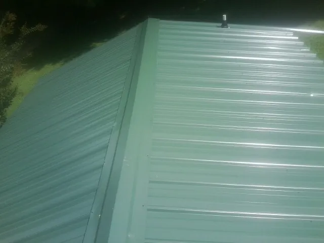 New green metal panels meeting at the ridge of a roof — Flat Roof Repair work by our crew in Shamokin Dam