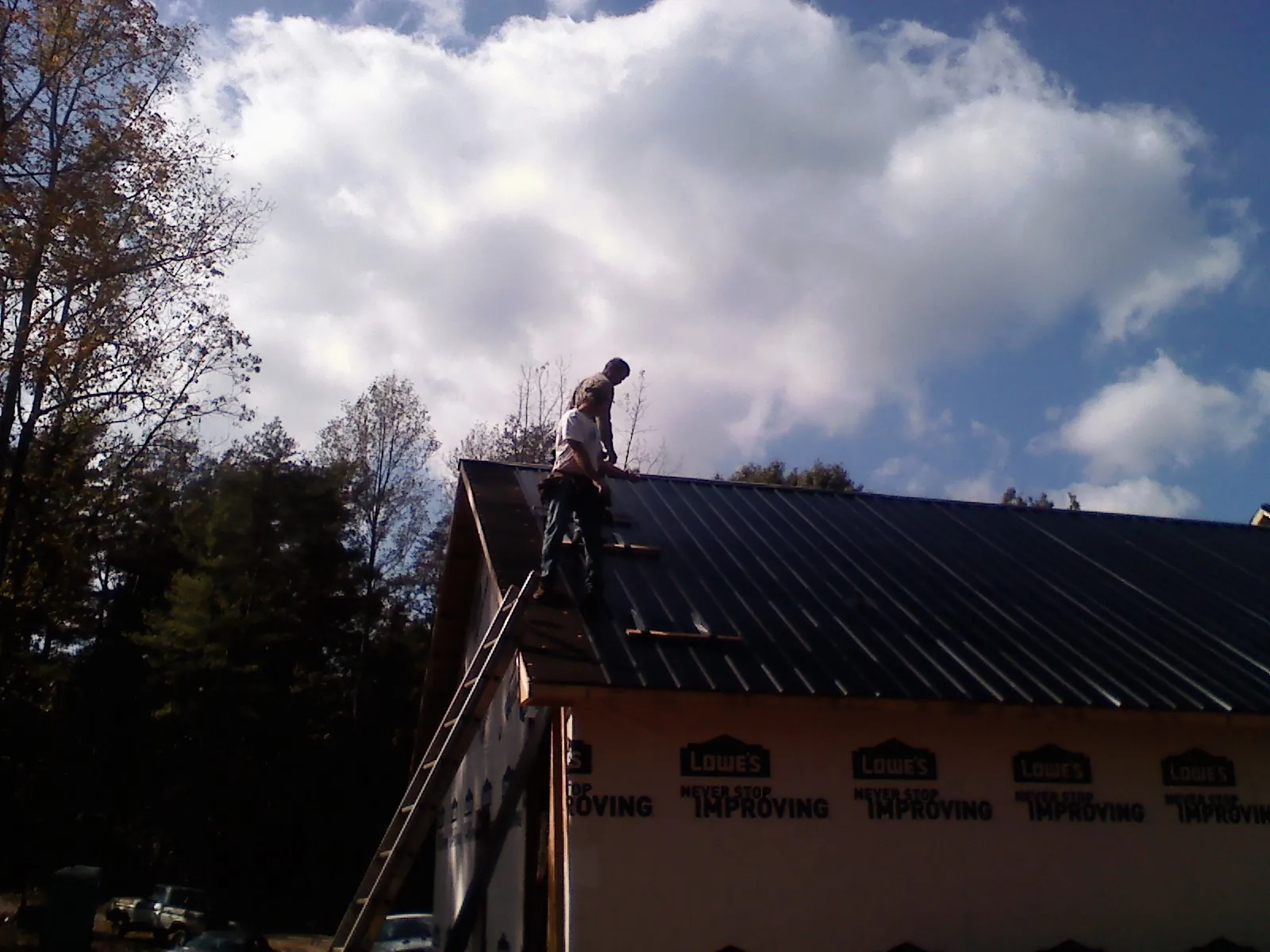Roofer fastening dark metal panels high against a cloudy sky, from a Roof Inspection job in Shamokin Dam