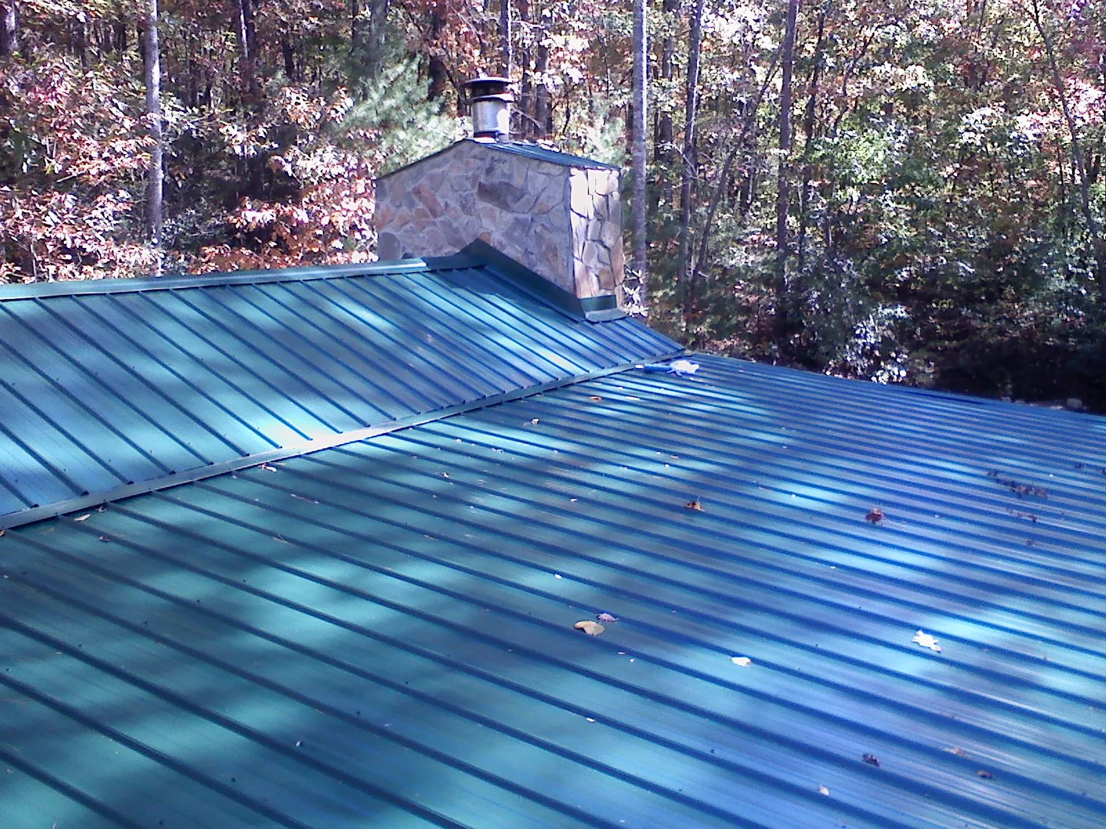 New green metal roof and stone chimney surrounded by autumn woods in Shamokin Dam