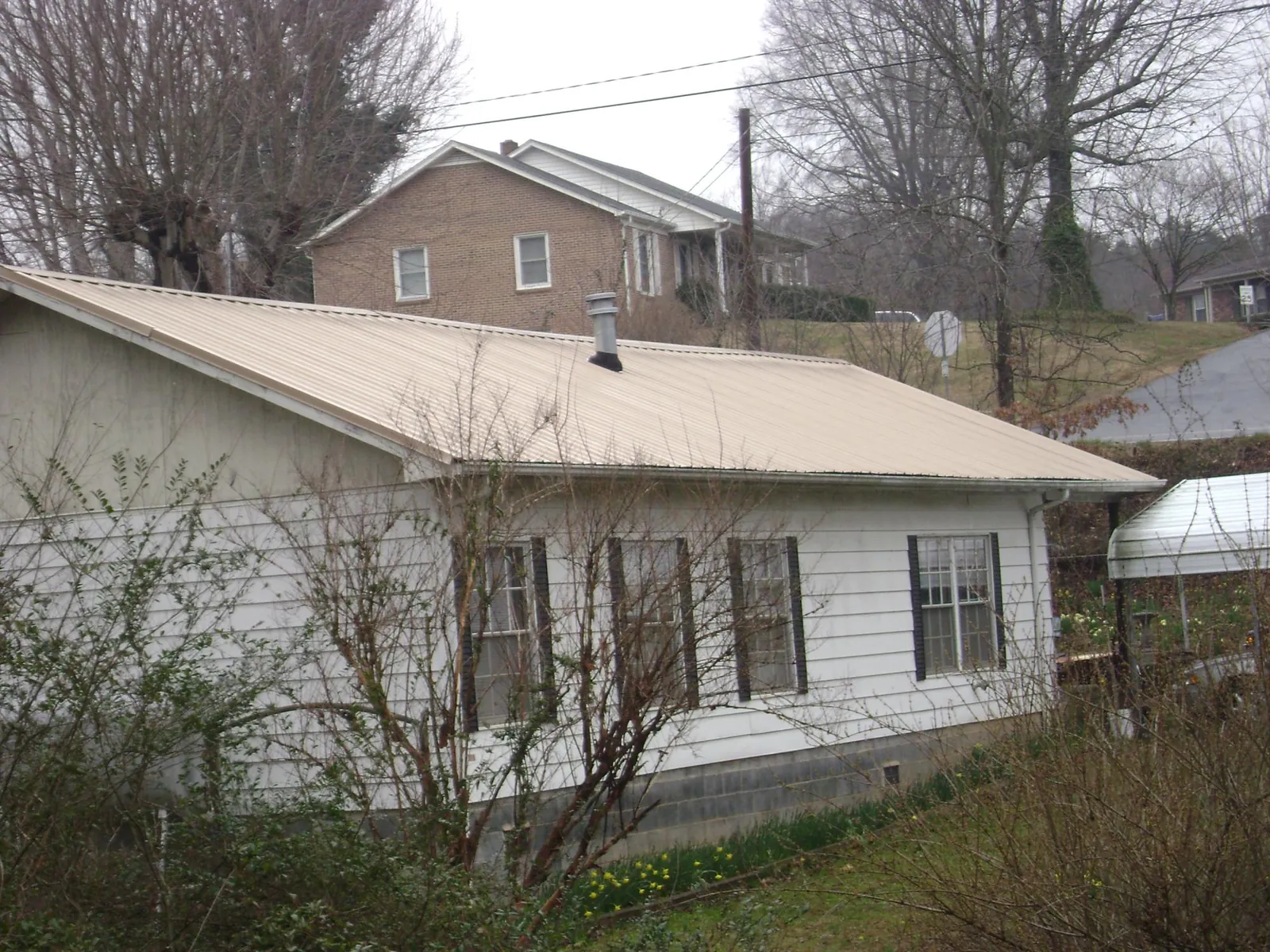 Tan metal roof on a white sided house set into a hillside — Commercial Roofing by Roofing Brothers in Shamokin Dam